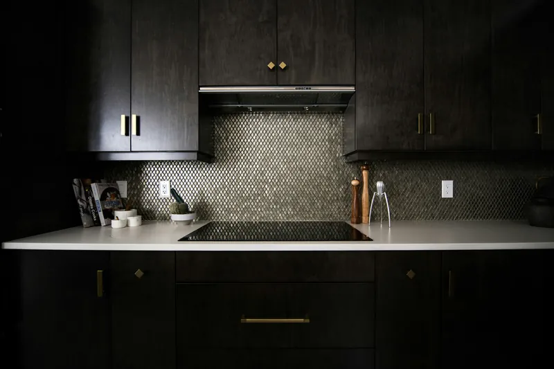 Dark stained cabinets with slim brass hardware framing a metallic diamond mosaic backsplash and a white worktop