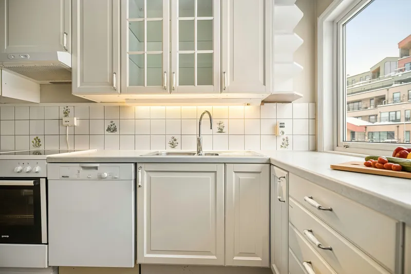 Dated white raised-panel kitchen with a floral-patterned tile backsplash and a rolled-edge laminate countertop