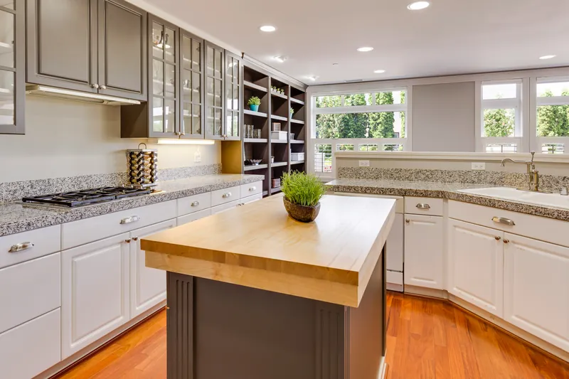 Grey glass-front upper cabinets over white lowers with granite counters and a dark island topped in thick butcher block