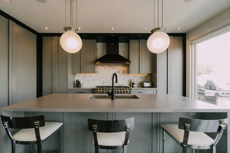 Grey shaker kitchen with a large concrete-toned peninsula, two glass globe pendants and a marble herringbone backsplash