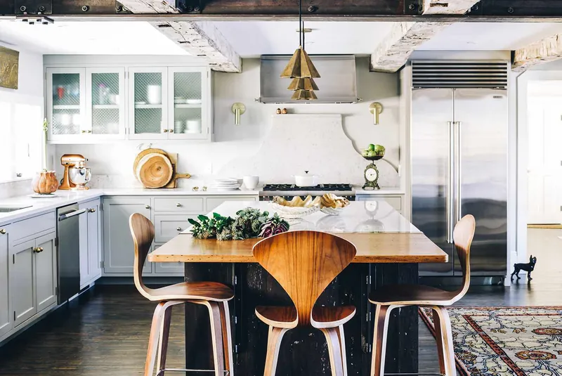Grey shaker kitchen beneath reclaimed timber beams with a brass geometric pendant over a wood-topped island