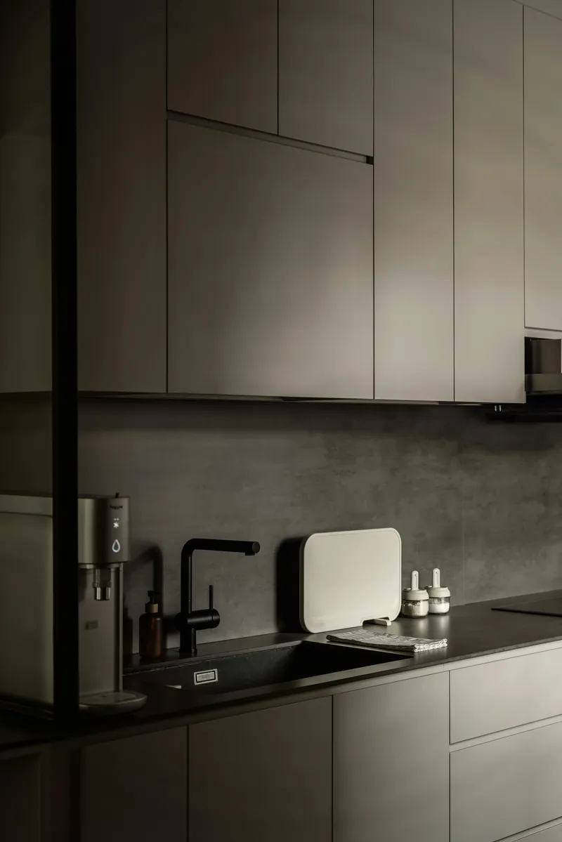 Handleless slab cabinets in soft greige with a dark stone worktop and matching splashback, a black tap and an undermount sink