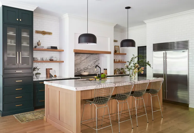Renovated kitchen with deep green tall cabinetry, white subway tile, floating oak shelves and a light oak island topped in veined marble