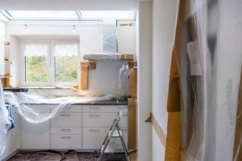 Kitchen part-way through a renovation with cabinets, counters and the range hood masked in plastic sheeting and paper