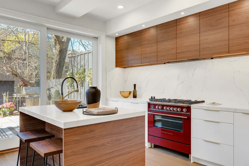 Walnut upper cabinets above white flat-panel lowers, a full-height marble slab backsplash and a deep red freestanding range