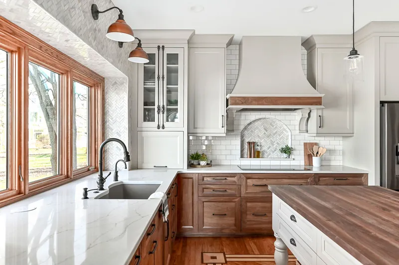 Walnut shaker base cabinets under cream uppers with marble counters, a herringbone marble backsplash and a custom plaster hood