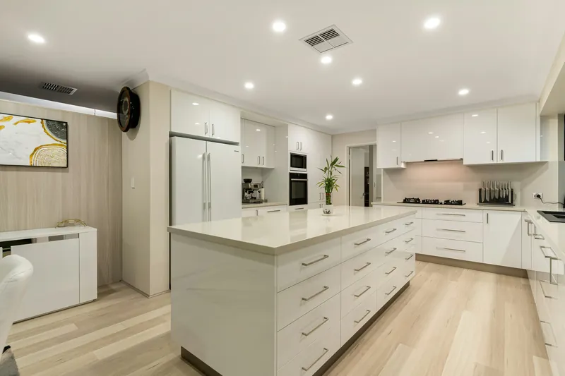 Bright white gloss kitchen with a long stone-topped island of deep drawers and pale timber flooring
