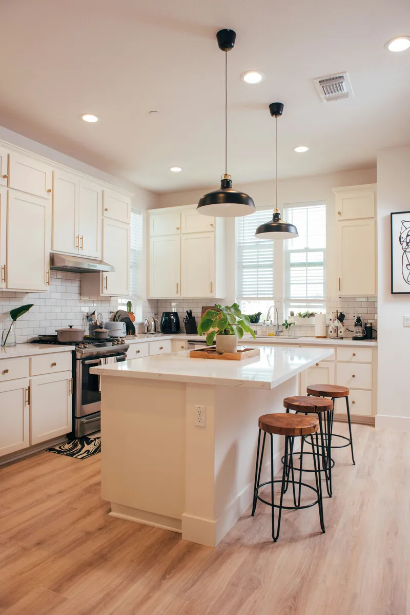 White shaker kitchen with a small quartz-topped island, two black barn pendants and wood-look plank flooring