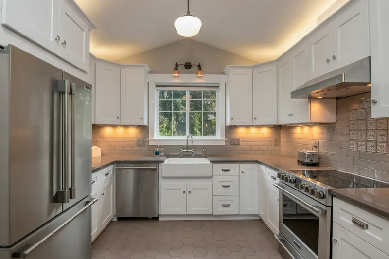 U-shaped white shaker kitchen with a farmhouse apron sink, grey quartz counters, taupe subway tile and hexagon floor tile